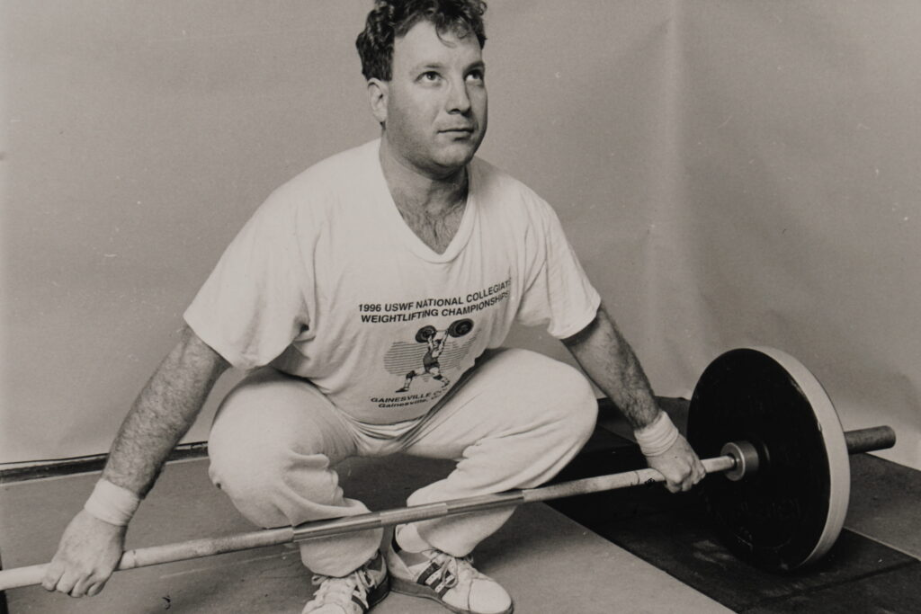 Lifter in frog-leg snatch starting position, gripping barbell